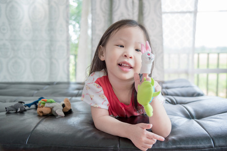 Little asian girl playing with animal puppets on sofaの写真素材