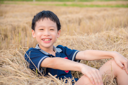 Young asian boy smiling in hay after rice field cultivedの写真素材
