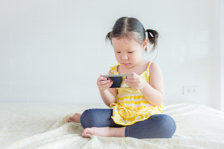 Little asian girl playing game on cellphoneの写真素材