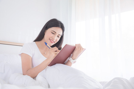Beautiful asian woman writing diary in bedroomの写真素材