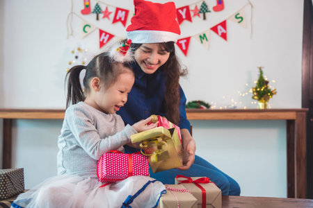 Little asian girl and her mother open christmas gifts box