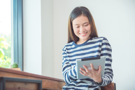 Beautiful young asian woman smiling while using tablet computer at homeの写真素材