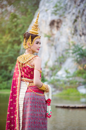 Beautiful asian woman wearing Thai ancient traditional costume holding flower ,standing near by the river and smilesの写真素材