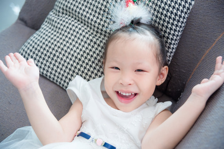Little asian pretty girl wearing white color dress lying and smiles on sofa at homeの写真素材
