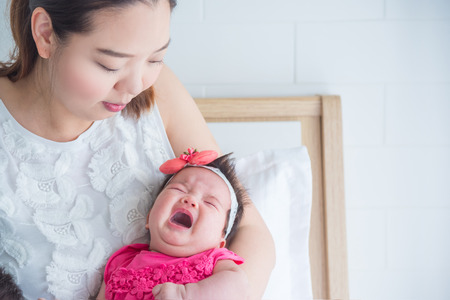 Little asian newborn crying while mother holding in bedroomの写真素材