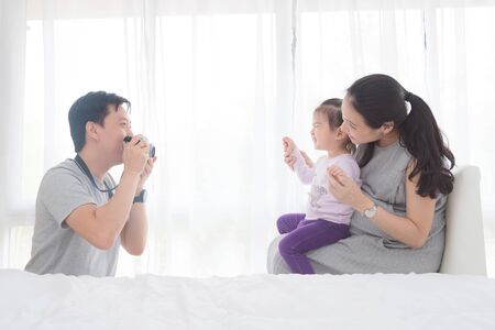 Asian man taking photo his wife and daughter by camera at homeの写真素材