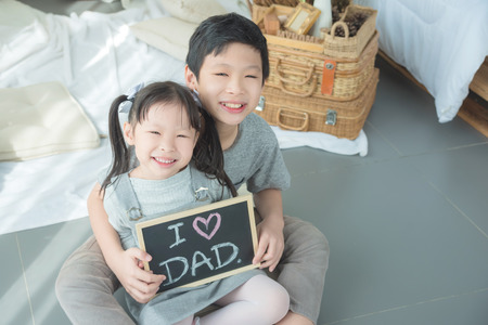 Asian children smiling while holding blackboard with text "I love dad"の写真素材