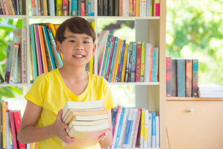 Young asian boy holding books and smiles in libraryの写真素材