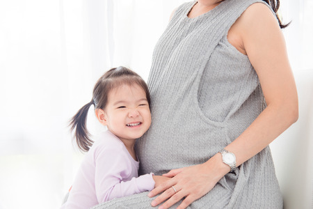 Little asian girl listening sound from her pregnant mother's bellyの写真素材