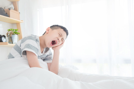 Young asian boy yawning on bed when he wake up in morningの写真素材