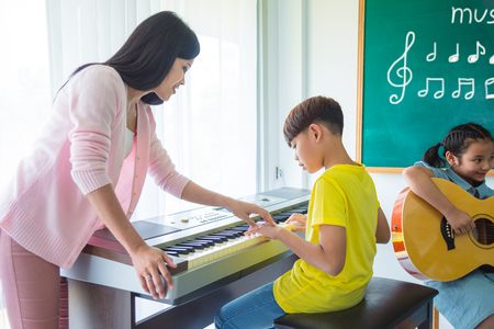Young asian boy playing music keyboard with his teacher in classroomの写真素材