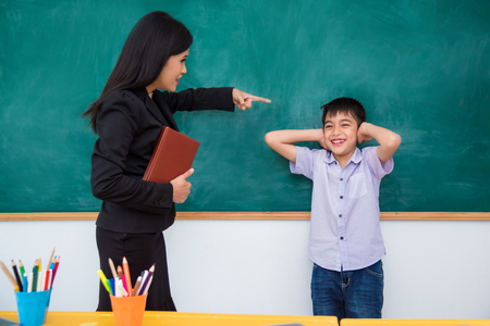 Asian schoolboy close his ears by hands and smiles while teacher scold himの写真素材