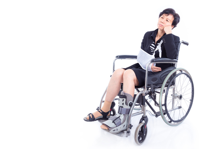 Asian businesswoman with broken arm and leg sitting on wheelchair over white backgroundの写真素材