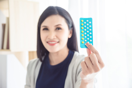 Asian beautiful woman holding contraceptive pills and smiles,focus at contraceptive pills.の写真素材