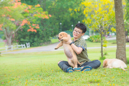 Young asian boy sitting and playing with his dog in parkの写真素材