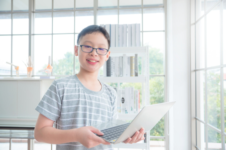 Young asian boy holding notebook computer at library and smiling at camera,education concept.の写真素材