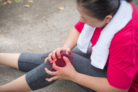 Asian aged woman suffering with knee ankle pain while running in park. Middle aged female sitting on the ground and holding painful ankle.の写真素材