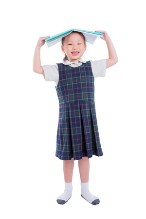 Full length of asian girl in uniform holding book and standing over white backgroundの写真素材