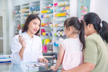 Beautiful asian Pharmacist explaining about digital thermometer to patient in drug storeの写真素材