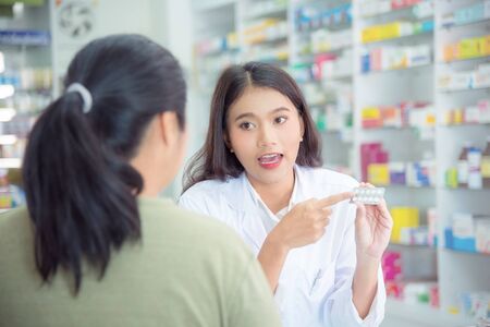 Beautiful asian Pharmacist explaining the pills to patient in drug storeの写真素材