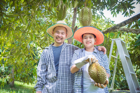 Asian farmer and son holding Durian and smile happily in their garden . Durian is a king of fruit in...