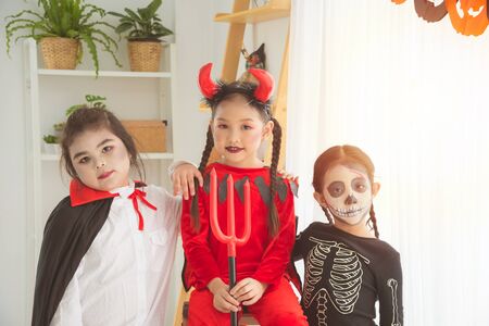 Group of little asian girls in Halloween costume standing and sitting together in room with Halloween decoration.の写真素材