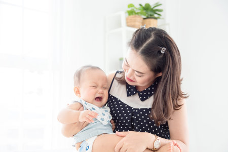 Beautiful asian mother comforting her little child between crying at home
