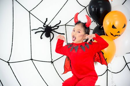 Pretty asian girl in red devil costume with horn sitting in room decorated for Halloween festival.の写真素材
