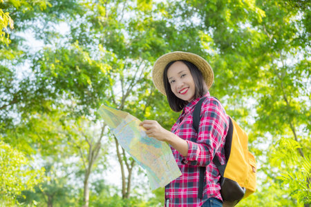 Asian traveler woman with backpack walking in the tropical forest,holding map and smiles at camera.