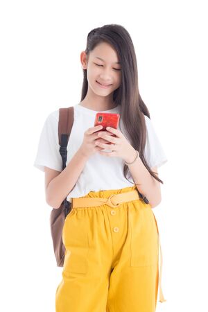 Beautiful asian teenage girl holding backpack standing and using smart phone isolated over white backgroundの写真素材