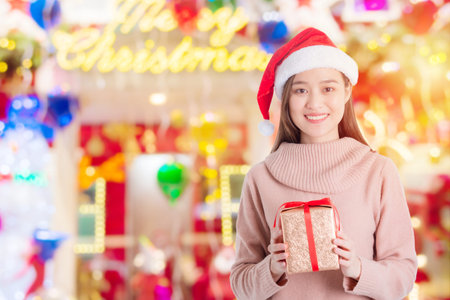 Beautiful asian girl wearing santa claus hat holding christmas gift box and smiles in room decorated for Christmas festival.の写真素材