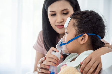Asian sick  girl with oxygen mask lying in bed at hospital and mother's hand holding together with daughter. Medical palliation healthcare concept.の写真素材