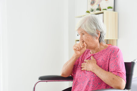 Asian senior woman sitting on wheel chair and coughing with out mask.の写真素材