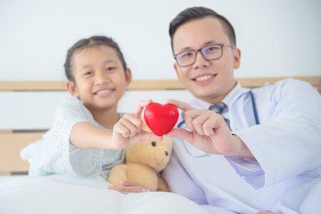 Child patient and male doctor holding red heart shape ball and smile together.の写真素材