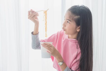 Young asian girl eating instant cup noodle by fork at home.の写真素材