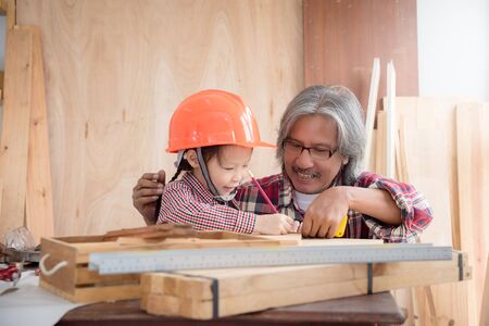 Senior male asian carpenter and grandchild making wooden house at home . Little asian girl working at carpentry workshop.の写真素材
