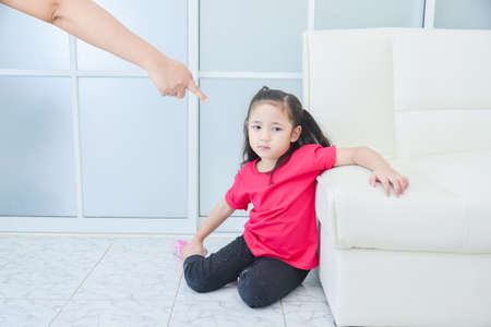 Mother pointing her finger to daughter while scolding her daughter at home.Sad girl sitting on the floor and scolded by her mother.の写真素材