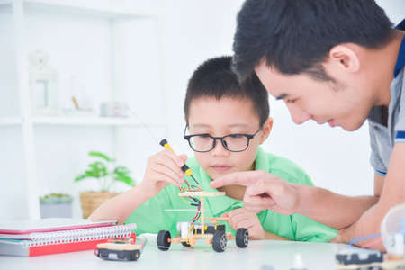 Happy boy helping his father while creating electric wooden toy car and enjoying time together in livining room at home.の写真素材