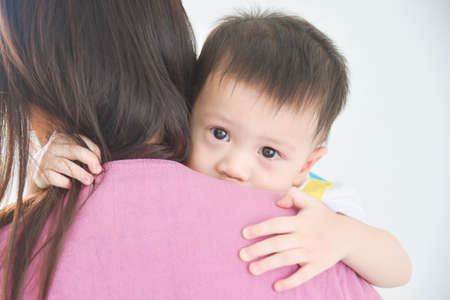 Close Up of Little Asian Boy with many tears on mother's shoulder.の写真素材