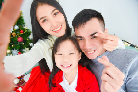 Beautiful asian mom, dad and daughter are doing selfie via smart phone and smiling while celebrating...