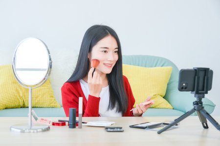 Young Asian female makeup artist , beauty vlogger or blogger recording  cosmetic makeup tutorial vlog by smart phone ,share on social media live streaming Internet.の写真素材