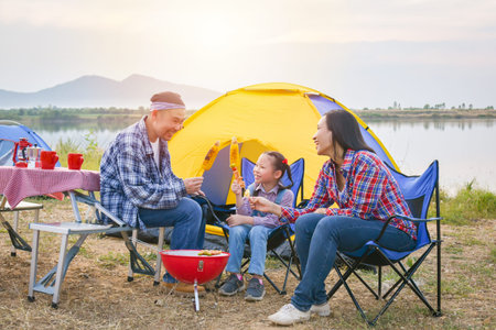 Group of asian family grilling sweet corn and BBQ on stove at camping site, everyone feeling happy. Family outdoor activity concept.の写真素材