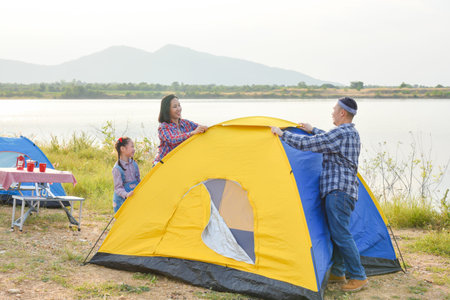 Asian parent with daughter setting tent by the lake. Family outdoor activity adventure on vacation.の写真素材