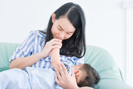 Beautiful asian mother breastfeeding her son on sofa at home.の写真素材