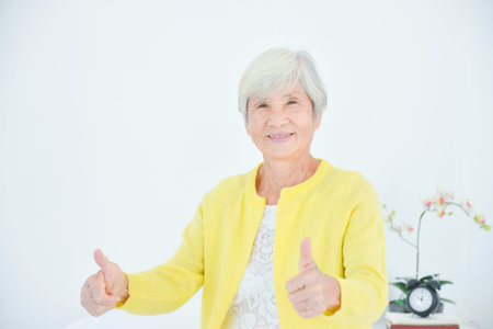 Female asian elderly with white hair smiling and showing thumb up at camera. Healthy senior concept.