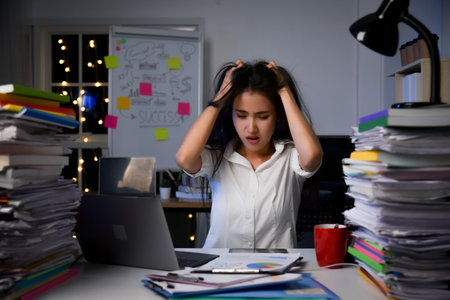 Stressed exhausted asian woman sitting at office desk and working overtime with overload work ducument on table.の写真素材