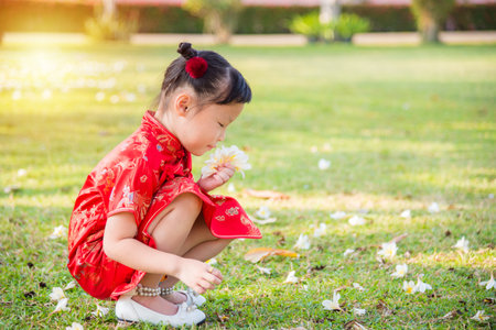 Little chinese girl wearing traditional dress holding flowers and smelling in park.の写真素材