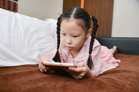 Little asian girl lying on sofa and using tablet computer.の写真素材