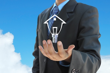 businessman hand holding a light bulb model of a house on skyの写真素材