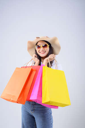 A beautiful Asian woman holding a multi-colored shopping bag with a happy expression on white background. Holiday Shopping.の写真素材
